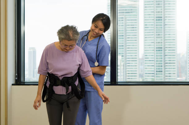 istock Woman physical therapist in blue uniform help an elderly to exercise and practice walking with Safety Transfer Belt. Atmosphere in Community Health Center. 1460718294