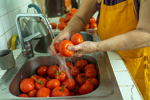 A woman washing tomatoes for tomato sauce preparation