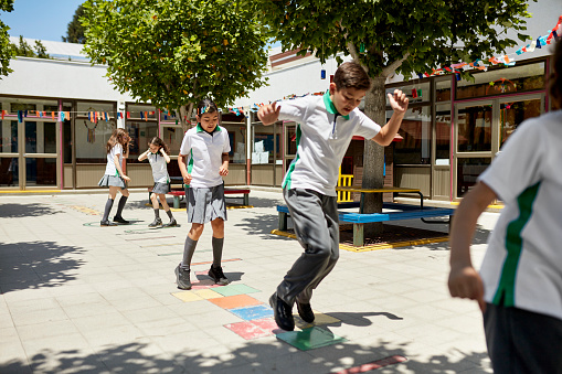 Full length view of pre-adolescent boys and girls in uniforms enjoying active games during recreation break.