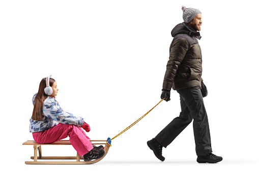 Full length profile shot of a father pulling a girl with a wooden sleigh isolated on white background