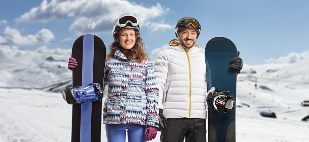 Young man and woman with snowboards posing on a snowy mountain