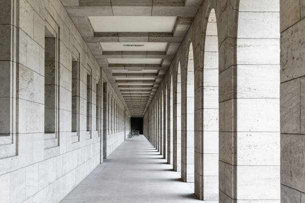 In an arcade of columns and windows, there are bicycles and a bike rack at the end.