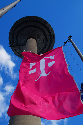 Frankfurt, Germany – May 21, 2021: The Deutsche Telekom flag seems to wrap itself around the shaft of Frankfurt's TV tower. Magenta and blue sky.