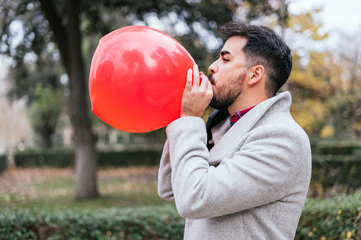 A shallow focus shot of a young male blowing a red balloon in the park