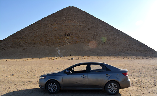 Giza, Egypt, January 26 2023: A car in front of The red north pyramid of Dahshur of king Sneferu, named for the rusty reddish hue of its red limestone stones, also called the bat pyramid, selective focus