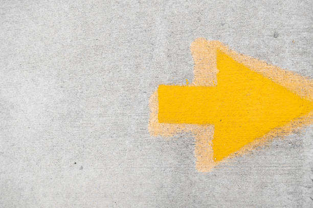 A yellow painted arrow pointing to the right on a concrete ground
