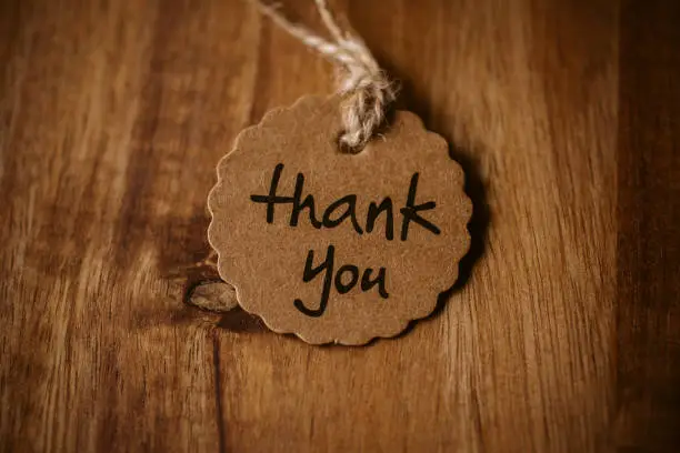 Photo of Thank you word written in a card on wooden background with selective focus.