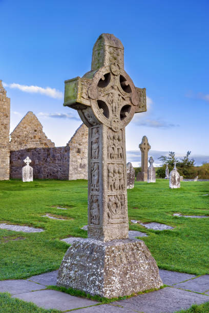 In an Irish cemetery, an ancient stone cross stands, weathered by time yet steadfast in its presence. Carved with intricate detail, it bears the weight of history and reverence. At its center, a solemn depiction of the sacred heart radiating with eternal love and compassion, serves as a poignant reminder of faith and remembrance.