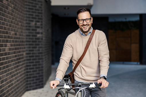 Portrait of a smart casual businessman standing on the street with his bicycle.