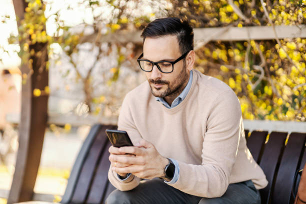 istock A serious man in smart causal is sitting on a bench outside and texting on his cellphone. 1460733464