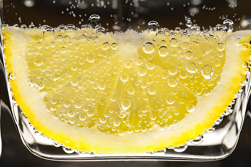 Lemon sliced in water with air bubbles, illuminated from below, close-up macro view, red citrus fruit