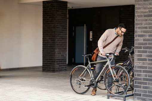A businessman in smart casual is parking his bike on the street.