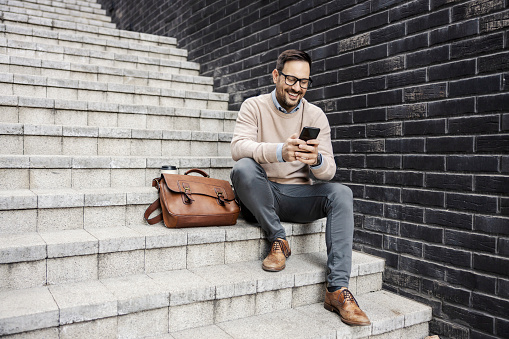 An executive in smart casual is sitting on the stairs outdoors and online chatting.