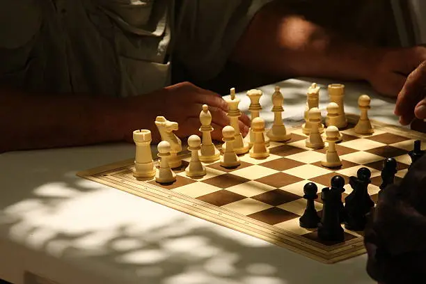 Chess board on a white table under a three with natural light.