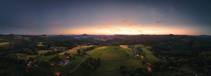 An aerial panoramic view of bright sunset cloudscape over the lush green village in the evening