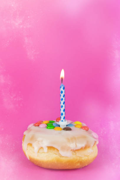 istock Birthday cake with a burning candle on a pink background 1460740095