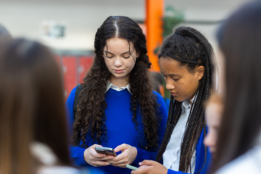 A waist-up shot of a group of teenagers on their phones looking down. They are all in school uniform in a school located in the North East of England.