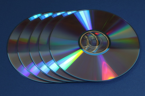 The five shiny compact CD and DVD discs on the dark blue surface