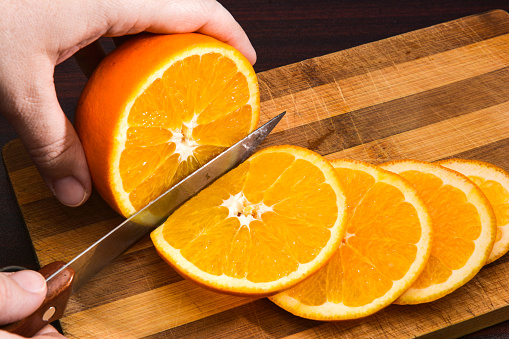 The Caucasian hands cutting orange on wooden board