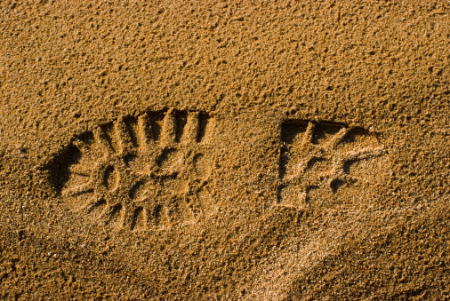 Foot print of a boot in the wet sand with strong shadows.