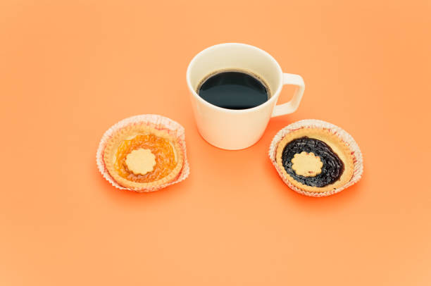 isolated apricot and cherry jam tart in a paper backing cup and cup of coffee on a orange background text space