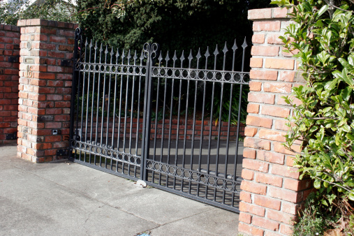 A close eletric iron gate, with three concrete brick pillars and a manual walk threw gate to the left