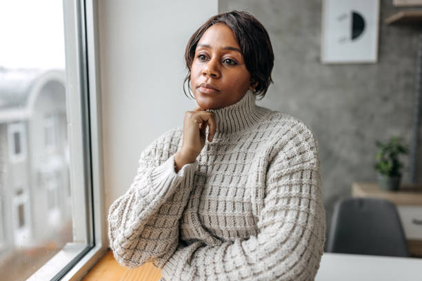 istock Young beautiful woman contemplating her thoughts while looking through window at her apartment 1460746274