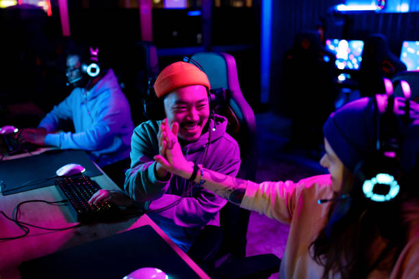 Happy Asian gamer congratulating his friend on winning in eSports. Happy Chinese gamer congratulating his friend on successful video game in entertainment club. esports stock pictures, royalty-free photos & images