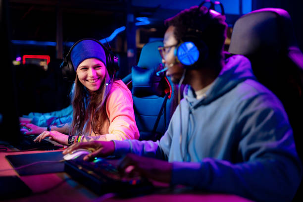 счастливые геймеры разговаривают во время игры в видеоигры в развлекательном клубе. - video game friendship teenager togetherness стоковые фото и изображе�ния