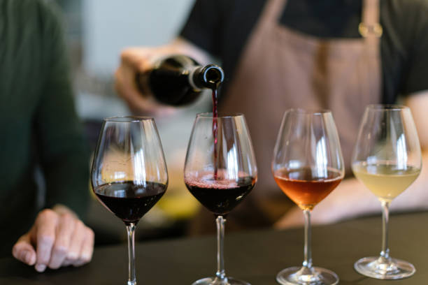pouring different wines into the glasses arranged for the wine tasting on the counter - garrafa de vinho imagens e fotografias de stock