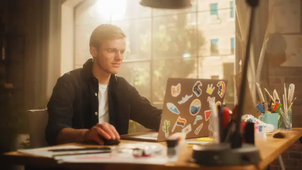 Photo of Concentrated Man Designs Video Game on His Powerful Laptop Computer in a Creative Office Space. Man Looking at Screen, Creating Digital Clothing and Footwear for Metaverse.