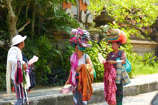 Street vendors selling sarongs on the street. Carrying stacks of sarongs stacked on their heads. Bali, Indonesia - 03.02.2018