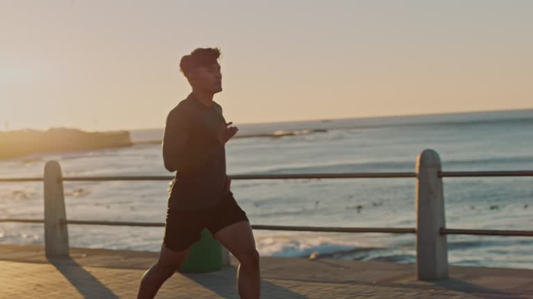 Man, music earphones or running by sunset beach, ocean or sea in healthcare workout, marathon training or cardio wellness. Runner, sports athlete or sunrise exercise with radio music in slow motion