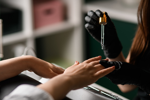 selective focus on pipette with nail care oil over female hand. Skin and nail care. Manicure. Beauty saloon