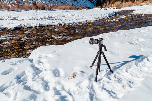 Digital camera on tripod taking picture of mountain river flowing in the Ala-Archa Nature Park in Kyrgyzstan during winter