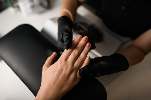 Manicure procedure in beauty salon. Master in black gloves and the hands of the client. Personal care and cosmetics. Close-up. Top view