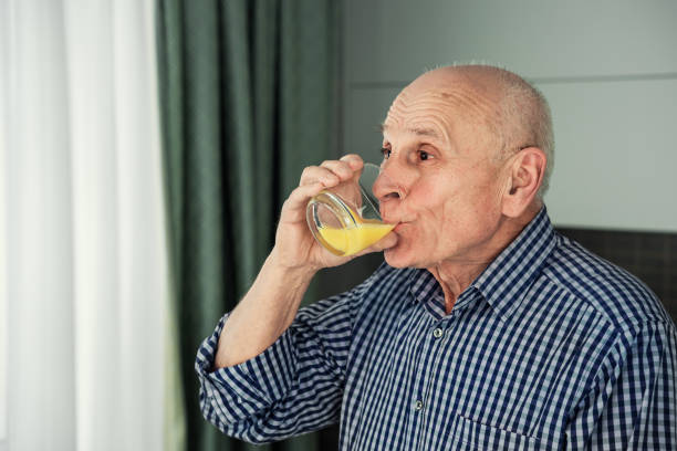 istock Old man drinking orange juice from glass close side view. 1460778252
