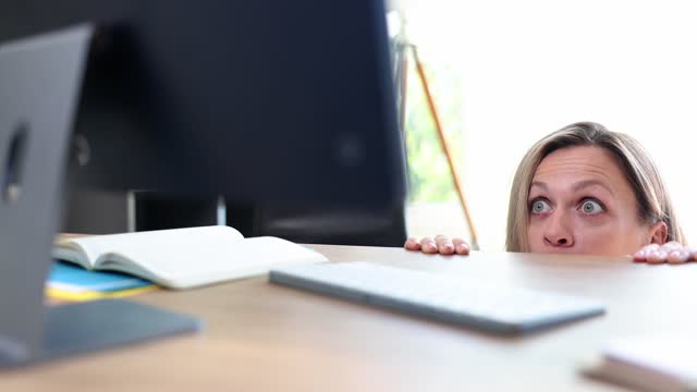 Shocked frightened female secretary peeking out under table and looking at computer screen 4k movie slow motion