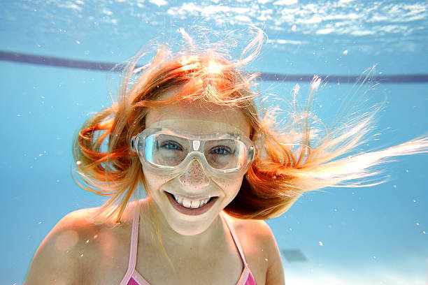 A young girl swims underwater in a pool.