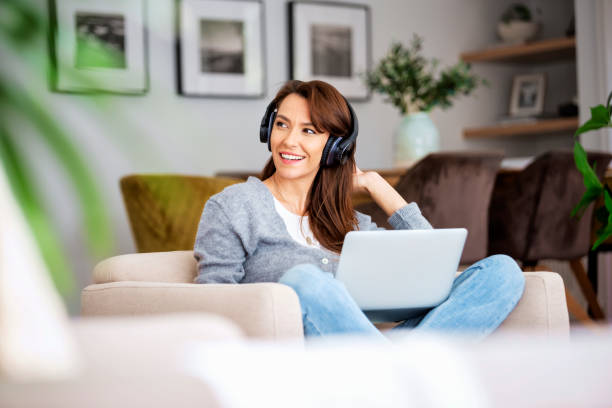 istock Happy woman wearing headphone and using laptop while relaxing at home 1460781180