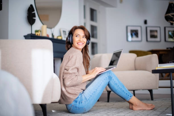istock Happy woman wearing headphone and using laptop while relaxing at home 1460781195