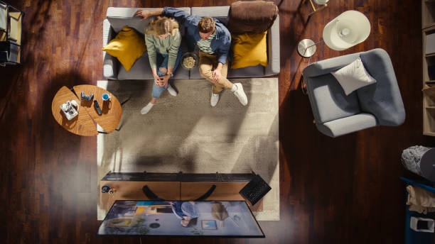 Top View Apartment: Happy Couple Watching Television in the Stylish Living Room. Looking at the TV Display and Eating Popcorn. Girlfriend and Boyfriend Enjoy Sitcom on Streaming Service on Couch. top view apartment: feliz pareja viendo la televisión en la elegante sala de estar. mirando la pantalla del televisor y comiendo palomitas de maíz. novia y novio disfrutan de comedia de situación en el servicio de transmisión en el sofá.