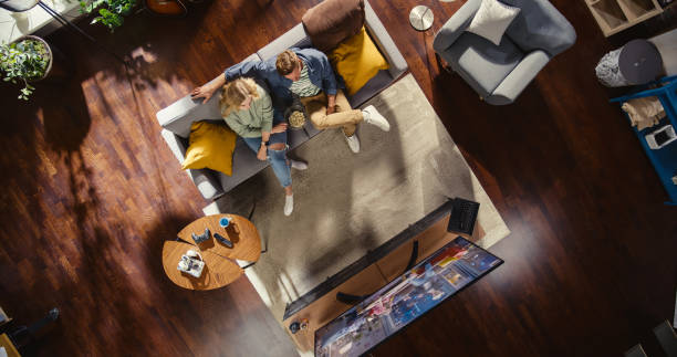 top view apartment: lovely couple watching television in the stylish living room. looking at the tv display and eating popcorn. girlfriend and boyfriend enjoy sitcom on streaming service on couch. - apartment television family couple imagens e fotografias de stock