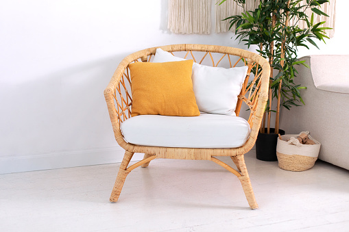 Design wicker chair in stylish light bedroom interior. Rattan armchair by the white wall in the living scandinavian room. Wabi sabi room interior. Eco natural furniture. Large green houseplant in pot