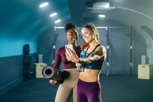 Two happy women in sportswear taking selfie in the gym after workout.
