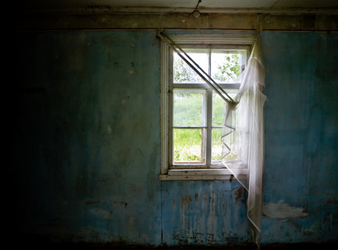 Inside abandoned house. View on broken window with curtain. Grunge scene.