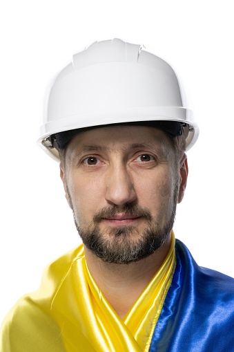 Portrait of a worker with a Ukrainian flag on his shoulders. The man with a work helmet on his head. Portrait of a man on a white background.