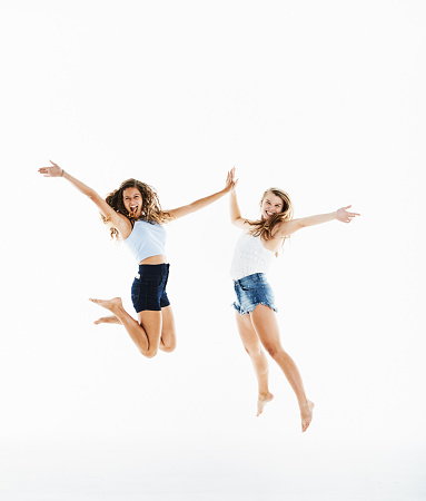 Teenage girl and young woman leaping against a white background, having fun and laughing.