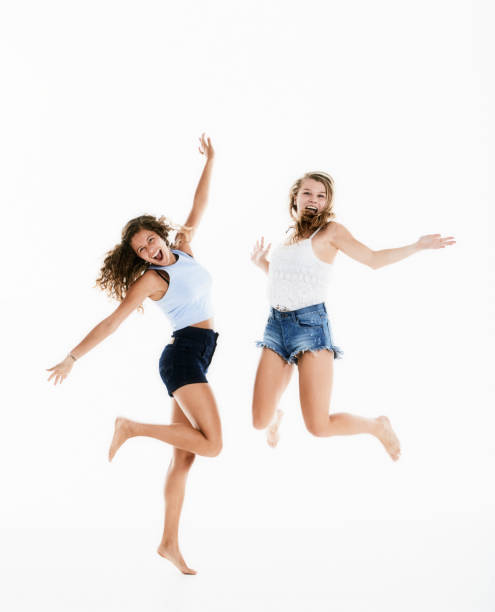 happiness! two young women leap gracefully into the air, smiling and laughing - arms outstretched teenage girls jumping flying imagens e fotografias de stock