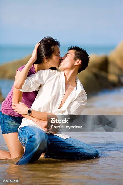 Amoroso Jovem Casal A Beijar Enquanto Squating Pela Praia - Fotografias de stock e mais imagens de Ao Ar Livre